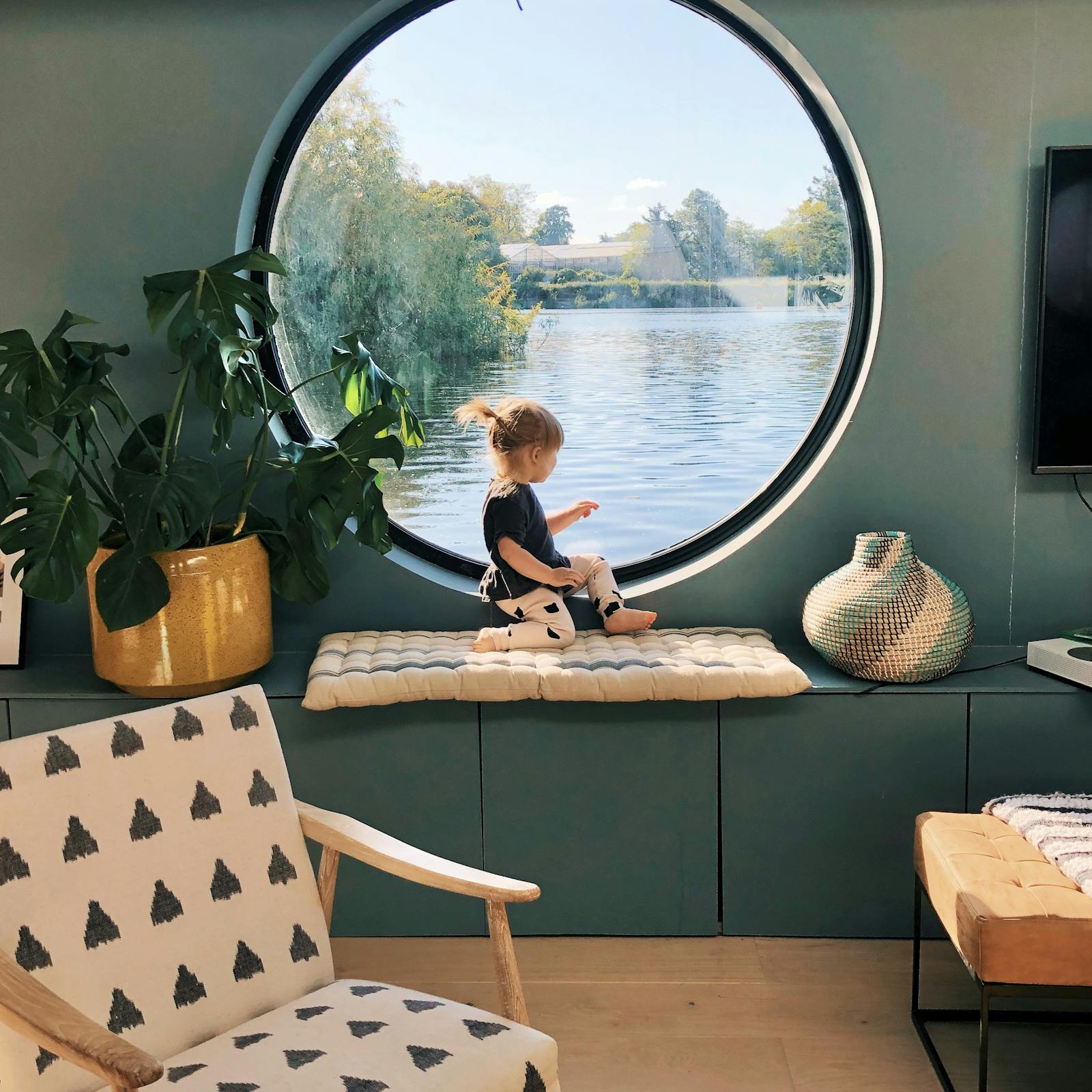 Child sitting in front of a large circular window in a teal painted living room