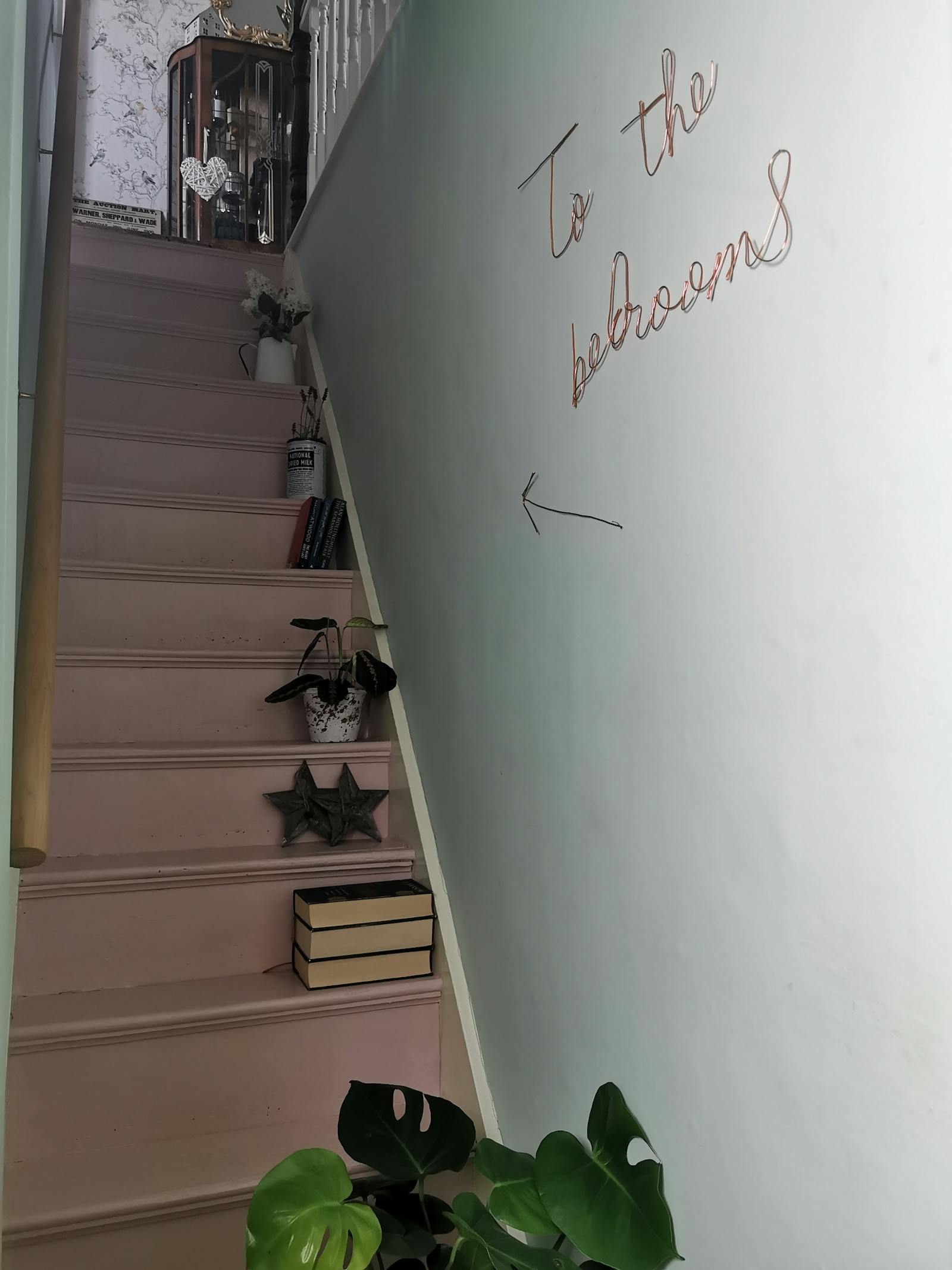 Narrow stairs painted in pink with a neon sign on the wall that says 'To the bedrooms'