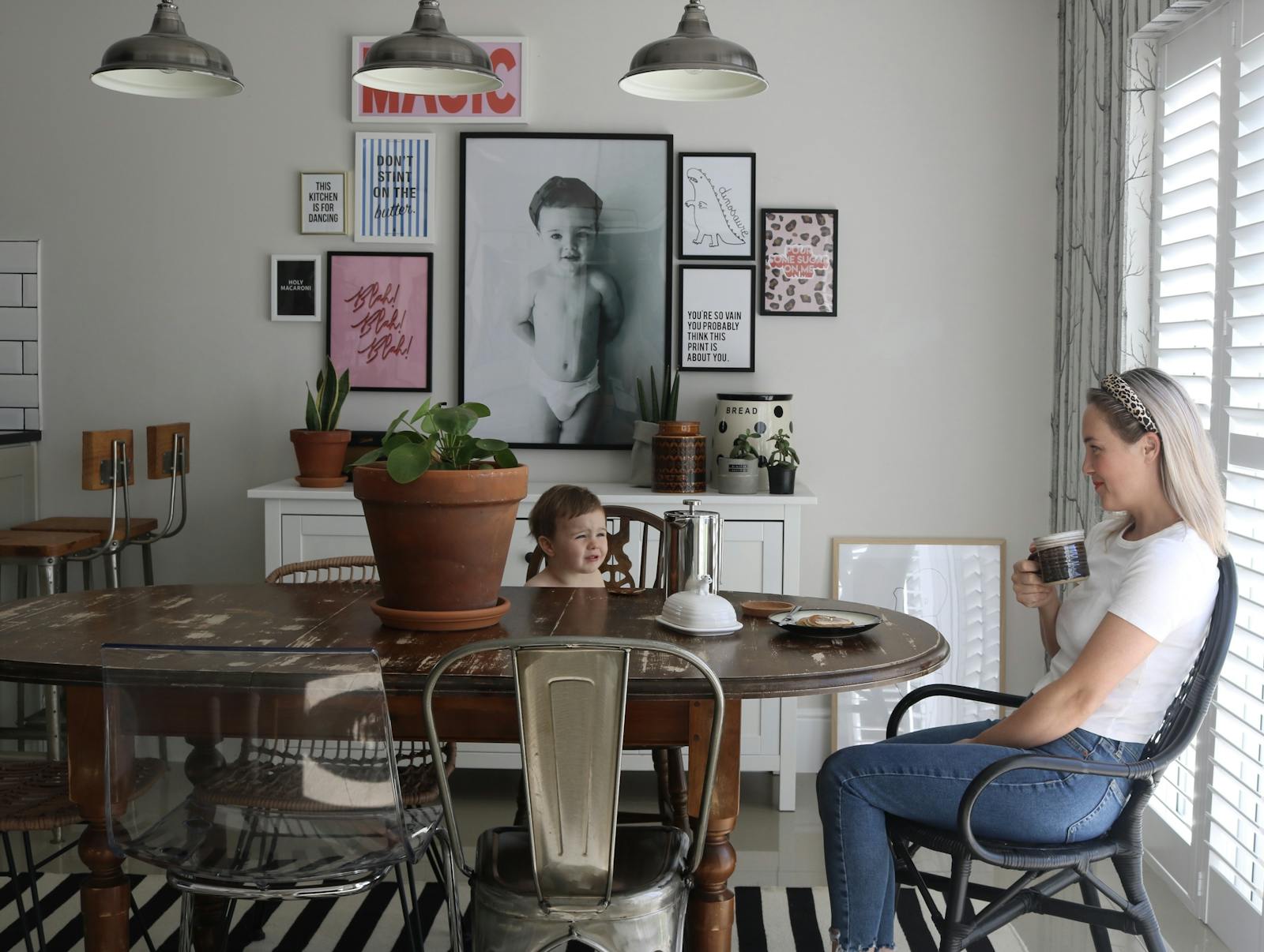 Photo of a woman and a kid in a dining room with photos placed on the wall behind them