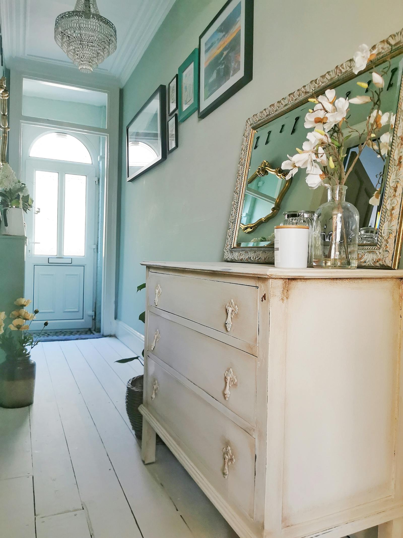A massive vintage chest of drawers painted in white, placed in a light green hallway with framed pictures on the walls