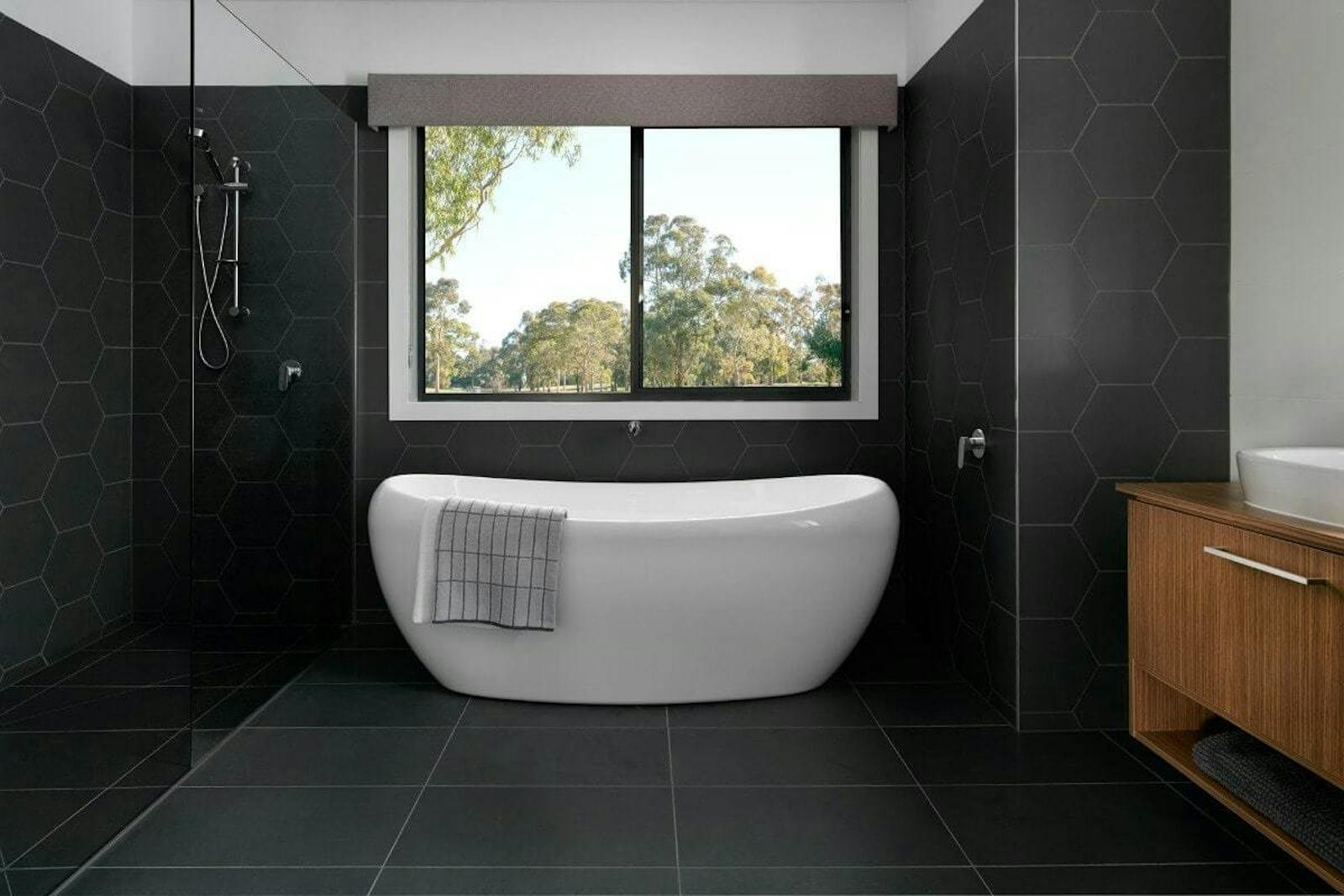 Black bathroom with big black tiles and a bathtub, placed in front of a big window