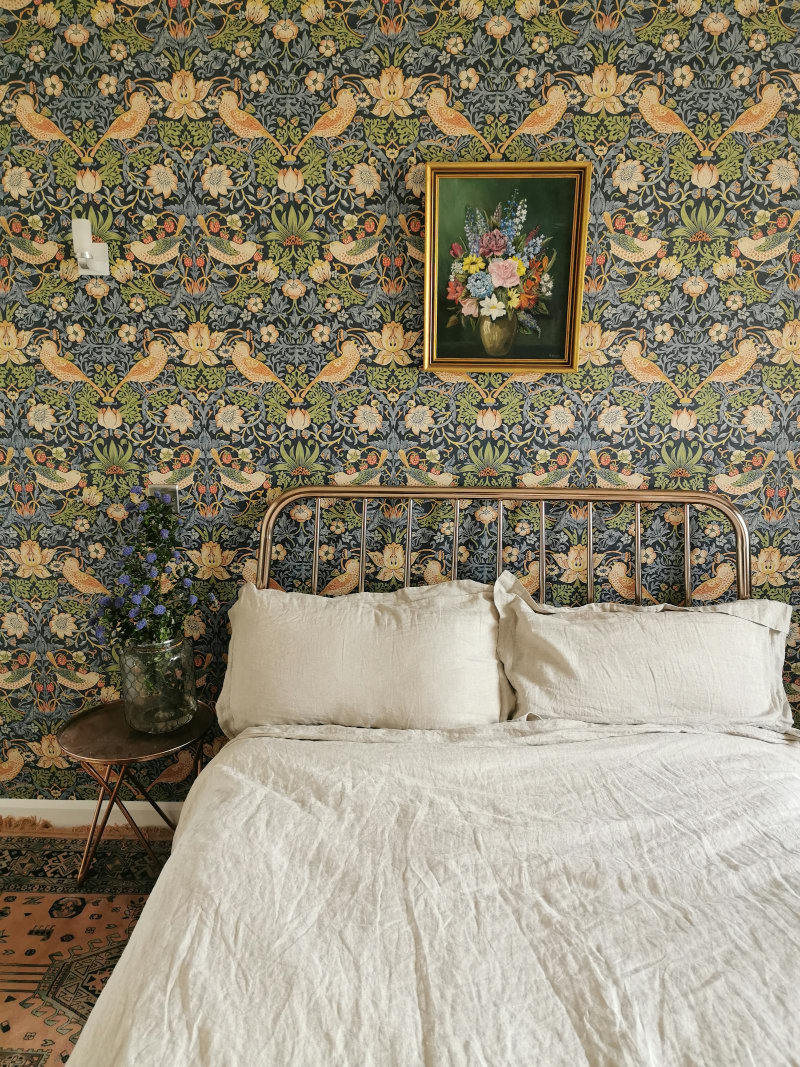 bedroom with patterned floral wallpaper behind it and artwork with flowers