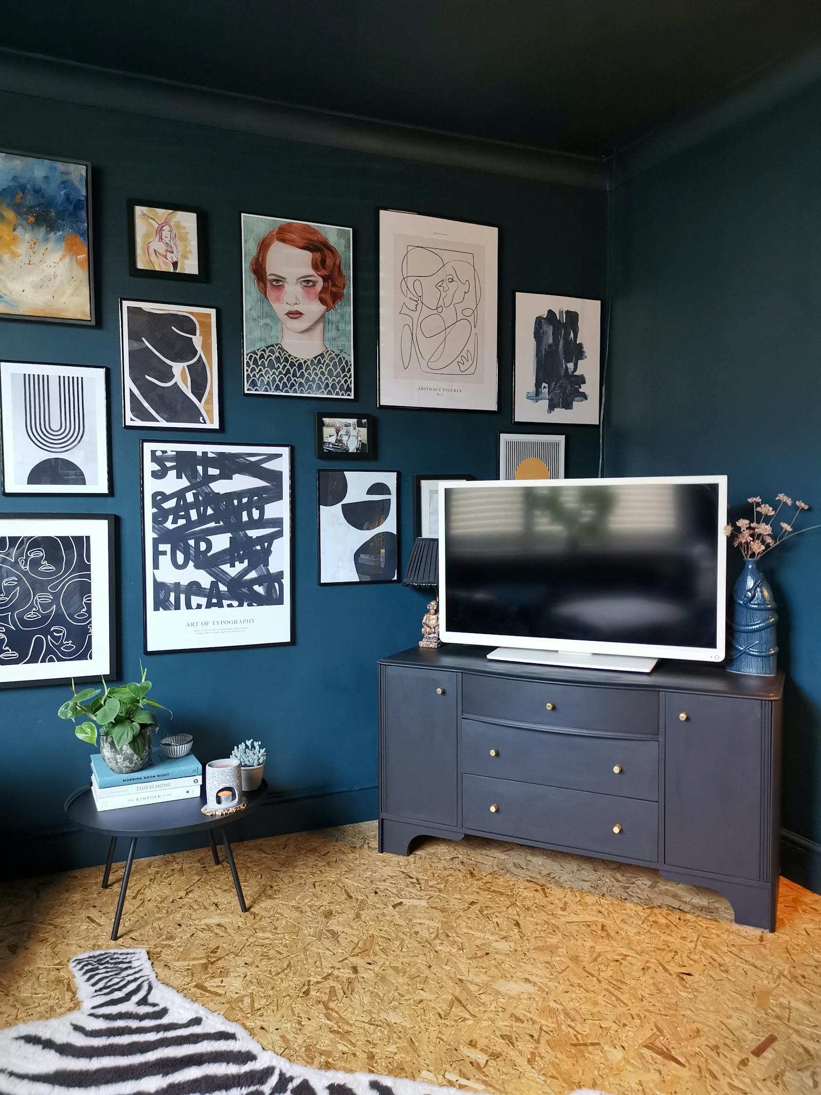 Living room painted in dark blue with a big gallery wall, cork floor and a tv stand with tv