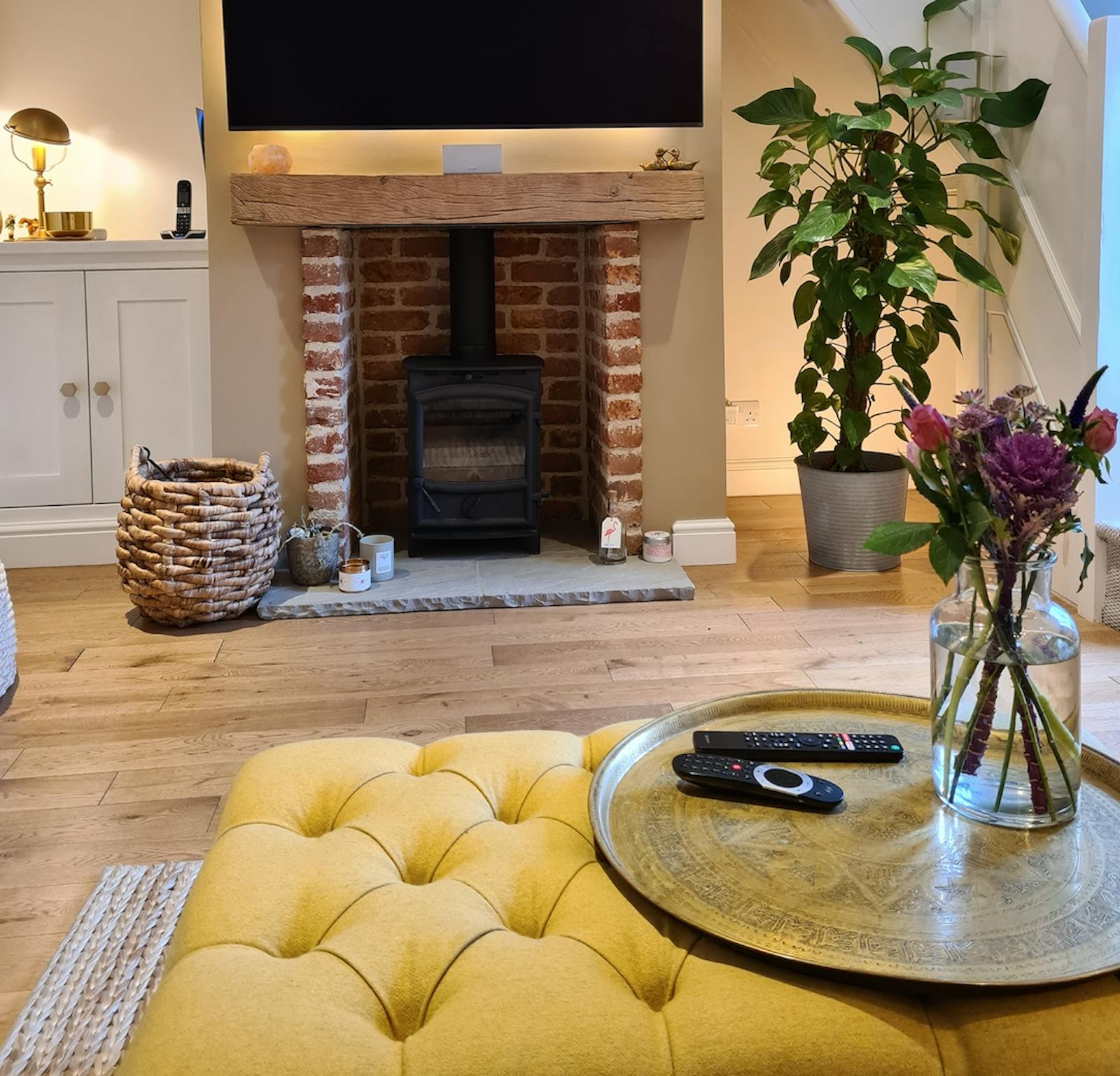 Living room with yellow foot stool, pink flowers and cosy fireplace