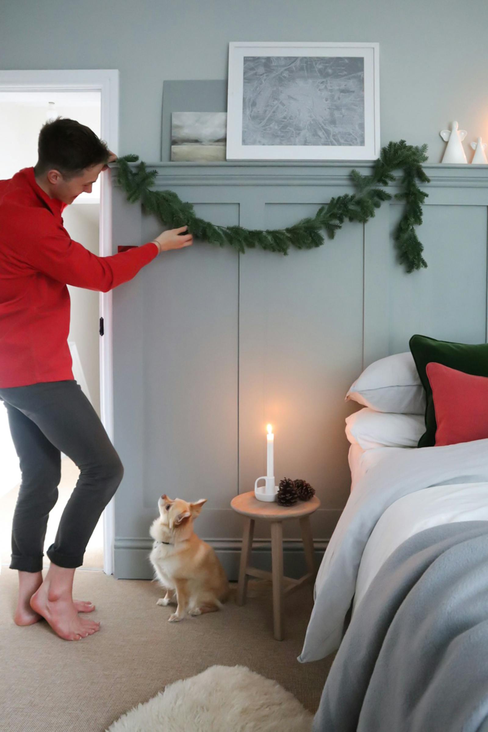 Man putting up Christmas decoration garland on bedroom wall above the bed