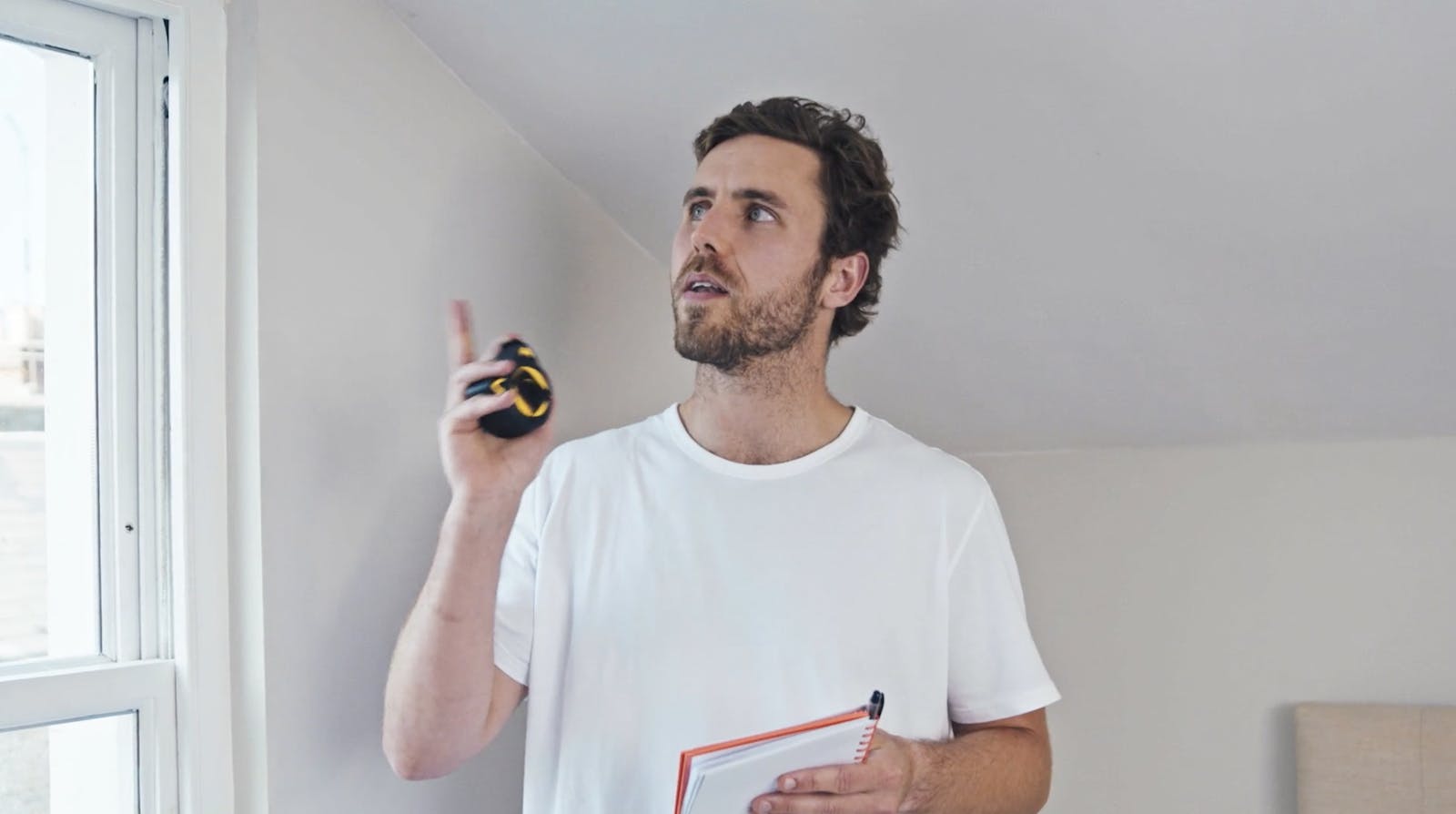Man holding metal tape measure pointing to a window