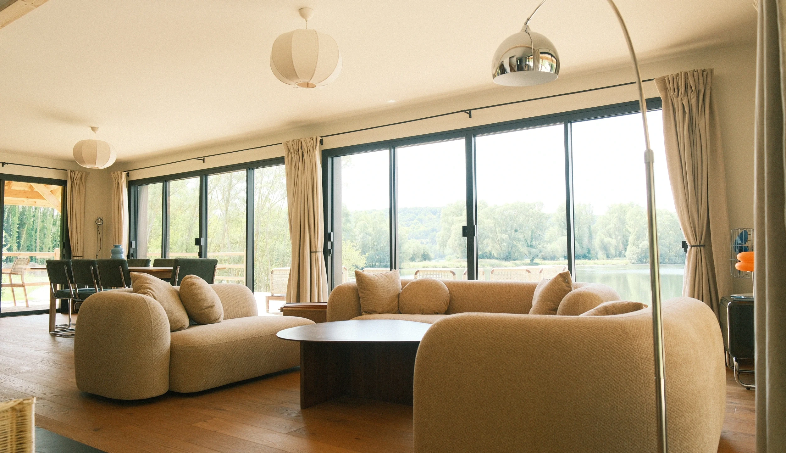 Dining and living area of the Canadian House, large central sofa, floor-to-ceiling windows with nature view