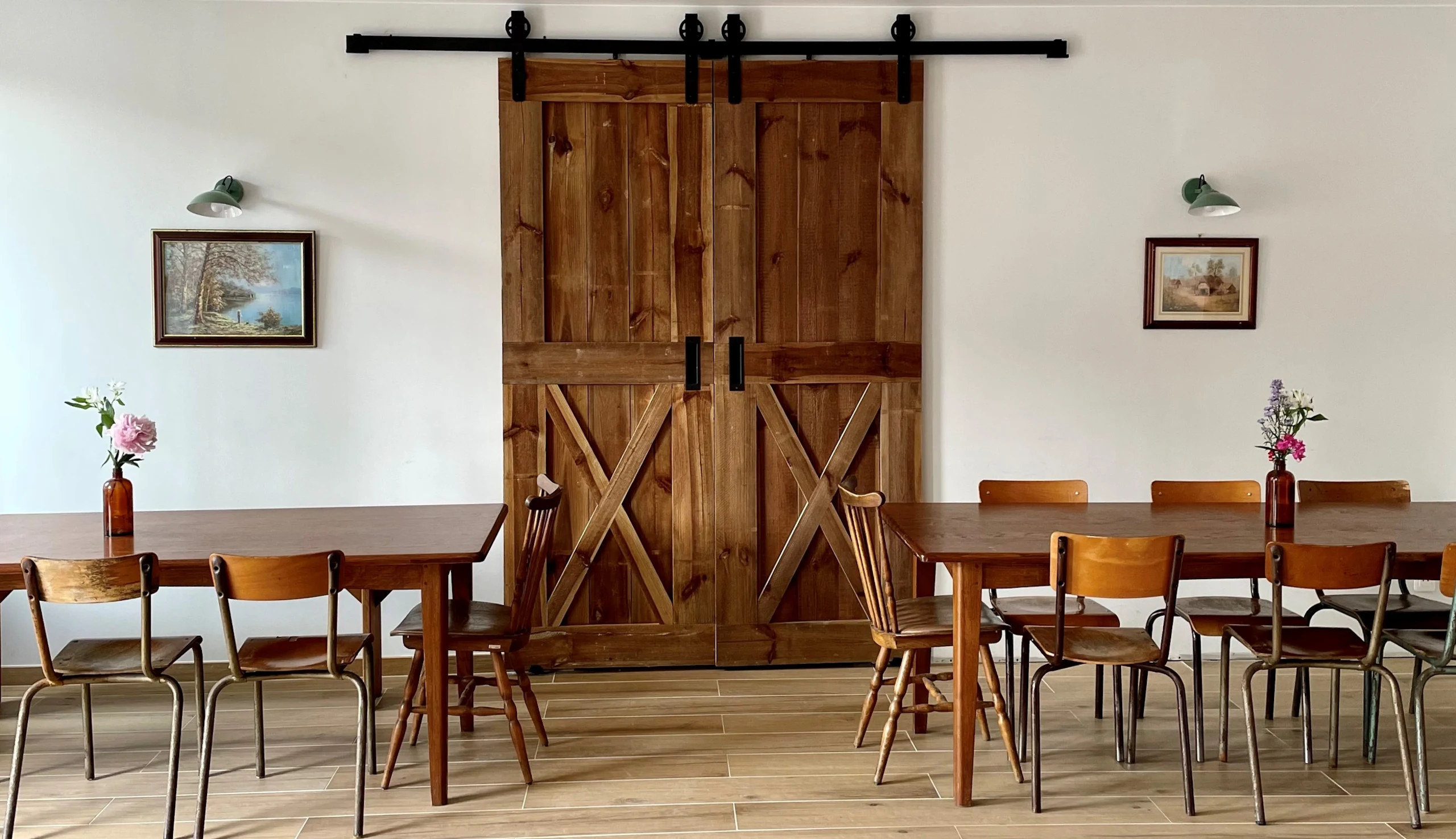 Dining room with two large wooden tables, large wooden barn door, two paintings