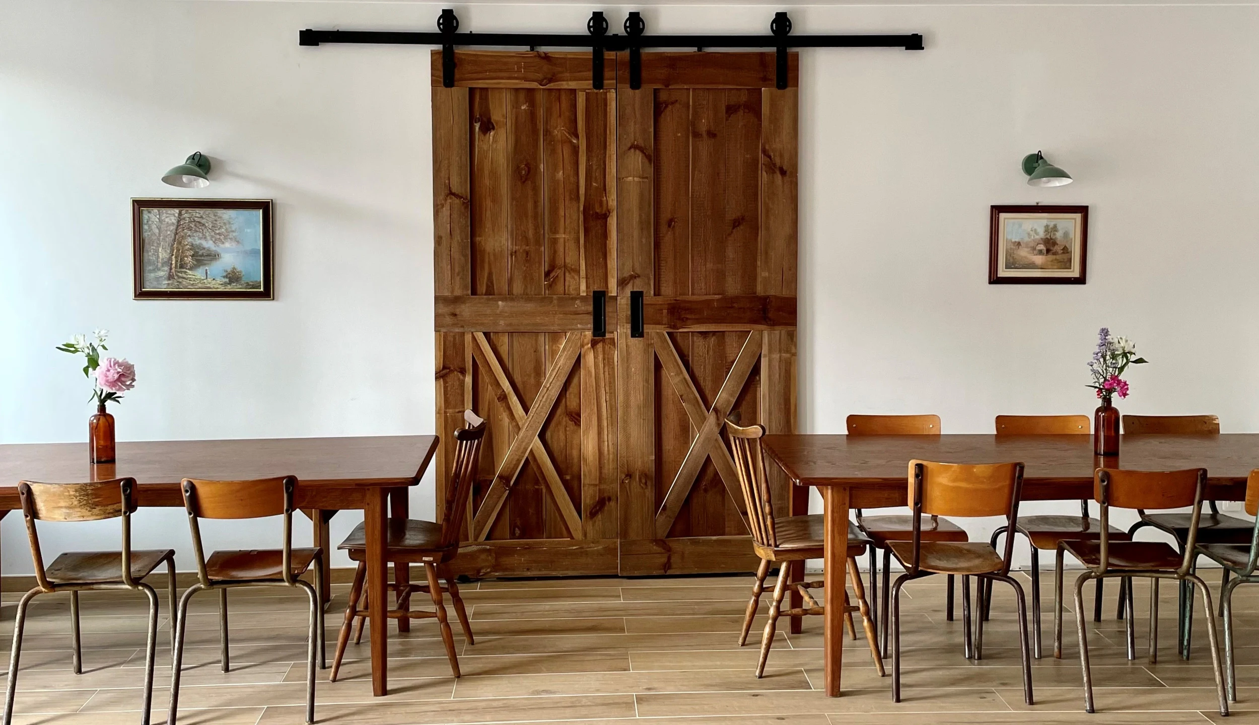 Dining room with two large wooden tables, large wooden barn door, two paintings