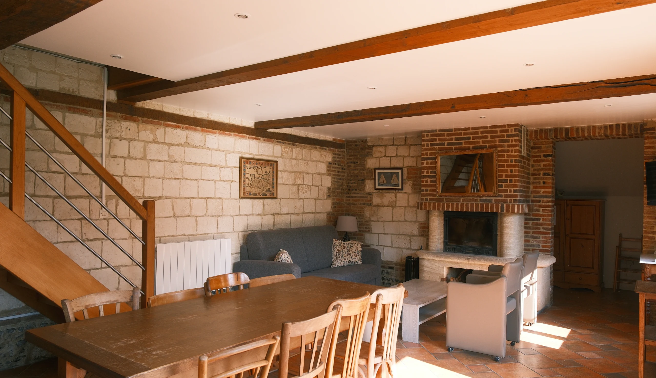 Dining room and living area with large dining table, sofa, armchairs, and stone fireplace