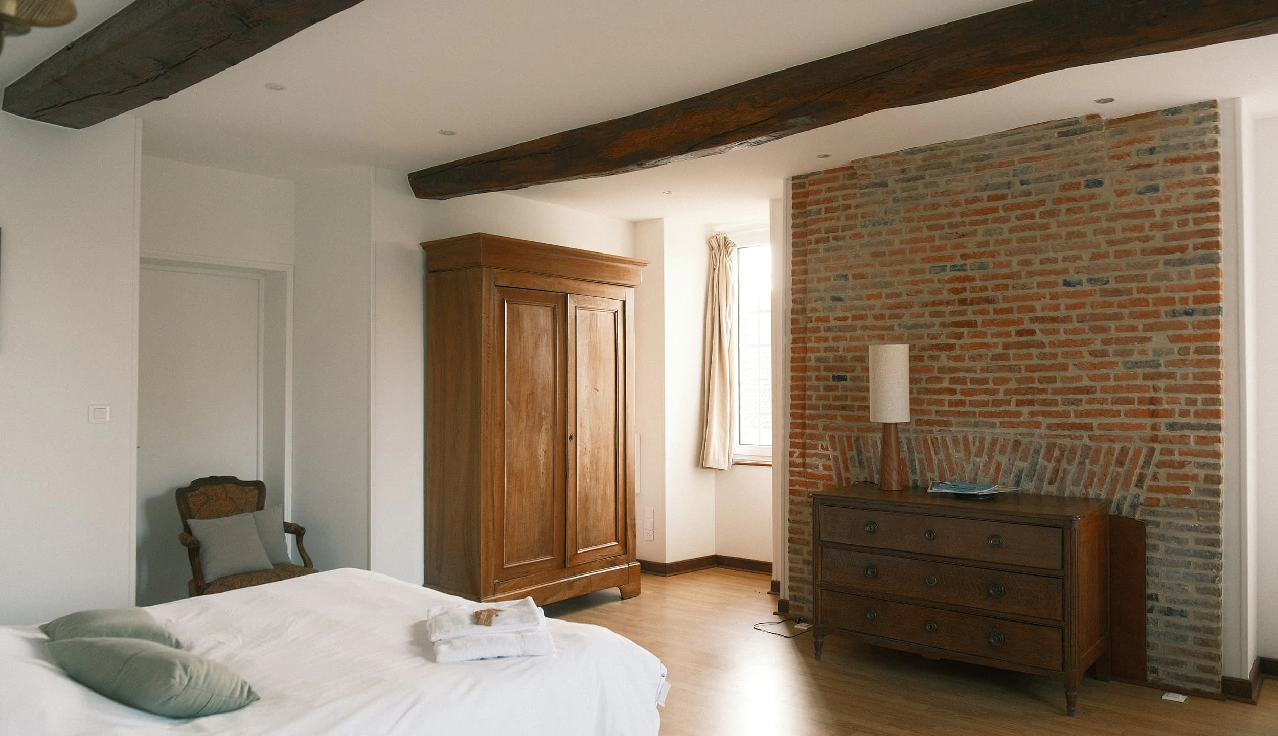 Bedroom with a double bed, a single bed, large wooden wardrobe and exposed brick wall