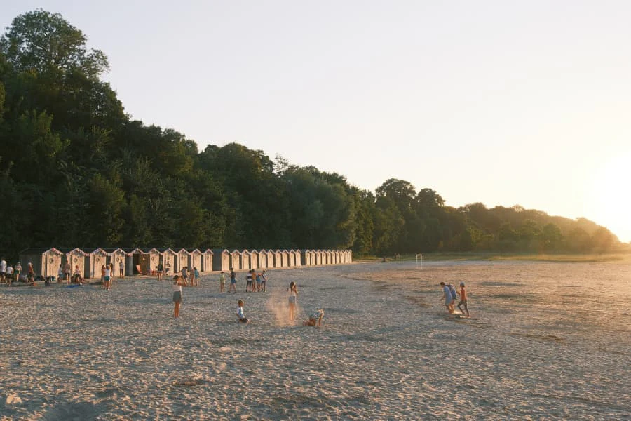 Plage de Saint Valery Sur Somme, des enfants cours sur la plage, on voit un couché de soleil et les cabines de plages.