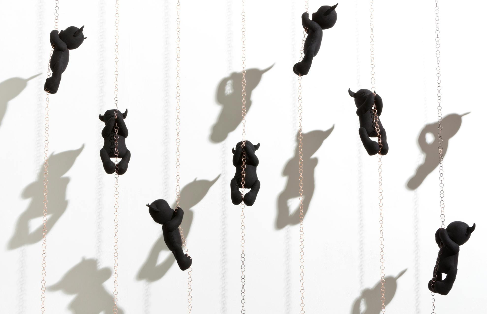 Black teddys climbing copper chains, creating shadows on the wall