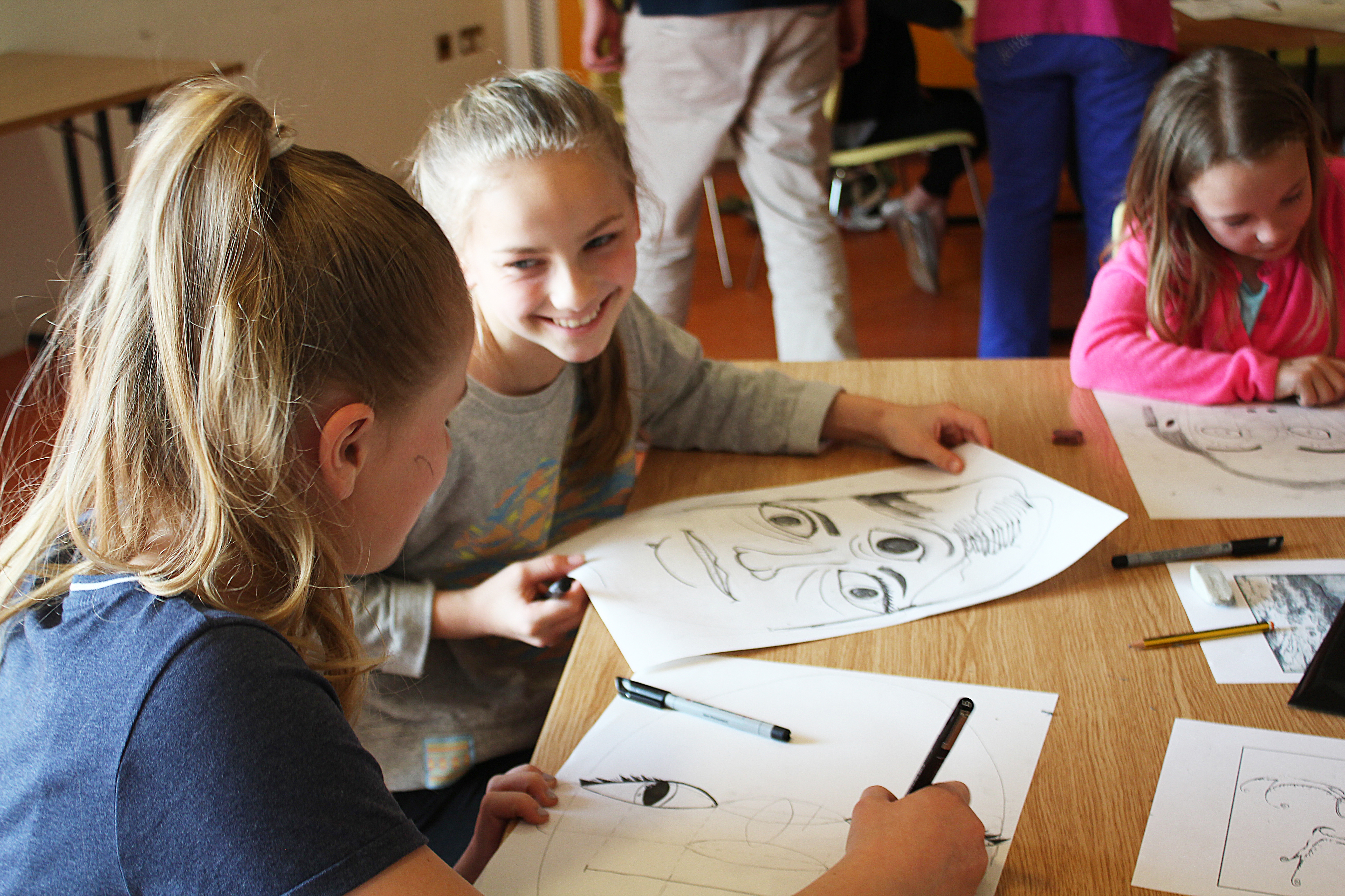 3 girls drawing faces on paper at a table