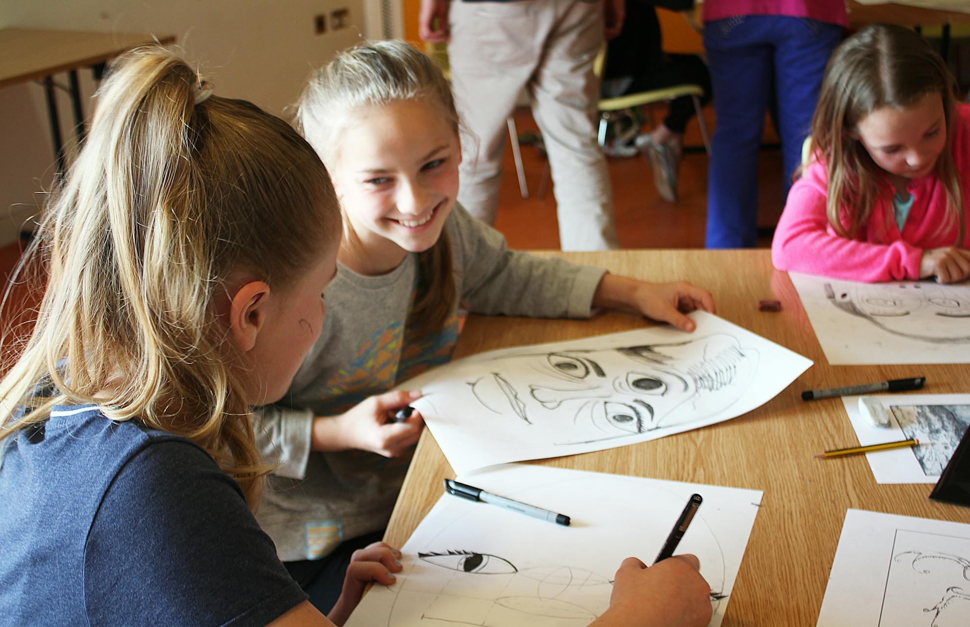 3 girls drawing faces on paper at a table