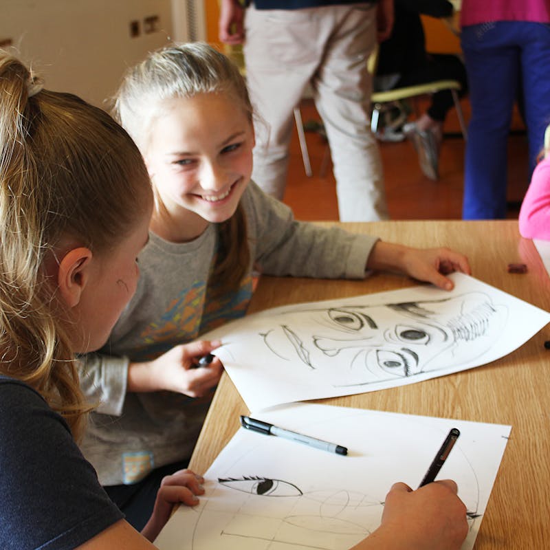 3 girls drawing faces on paper at a table