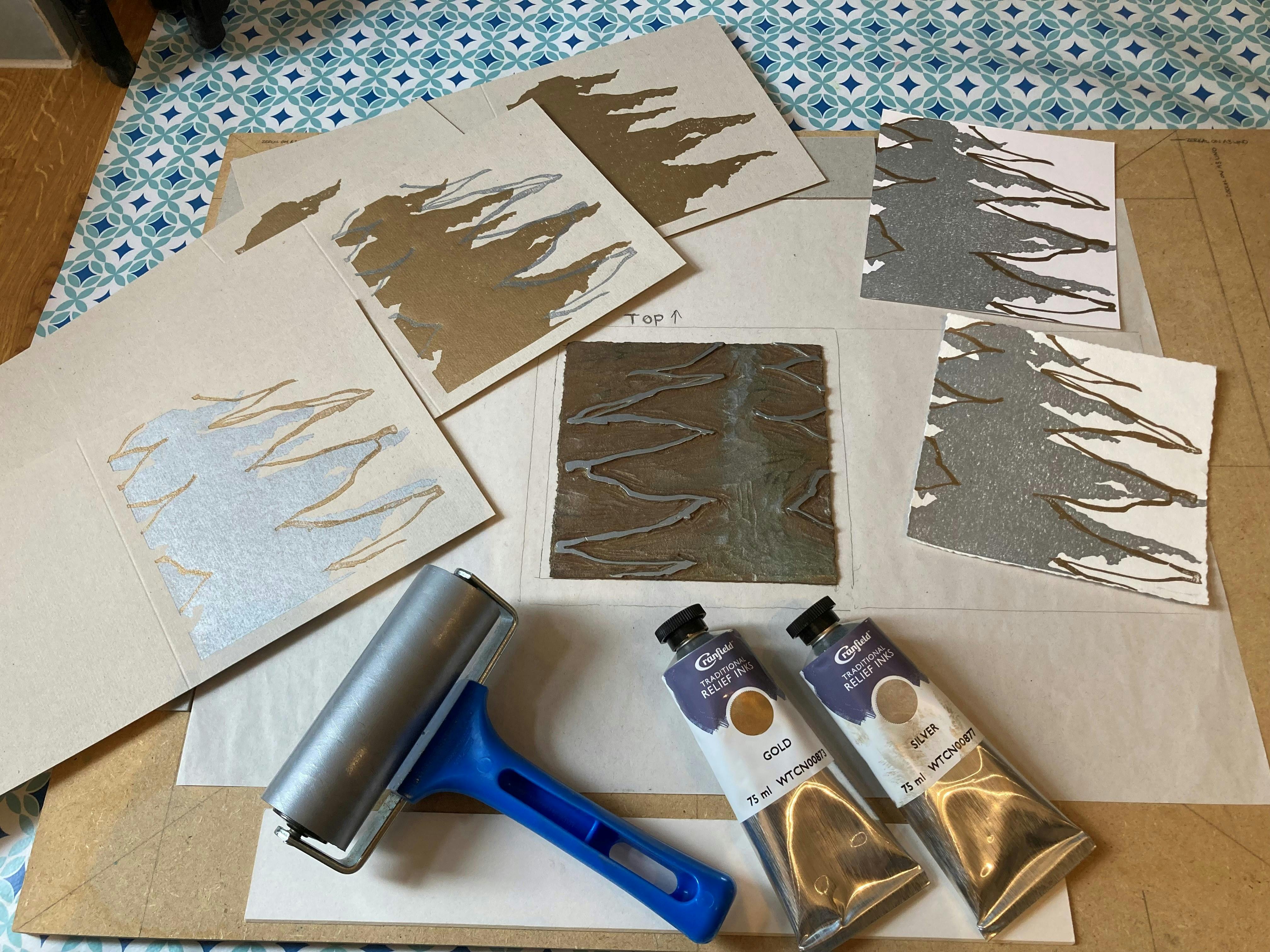 Image shows printmaking equipment including inks and roller with a piece of lino and paper prints