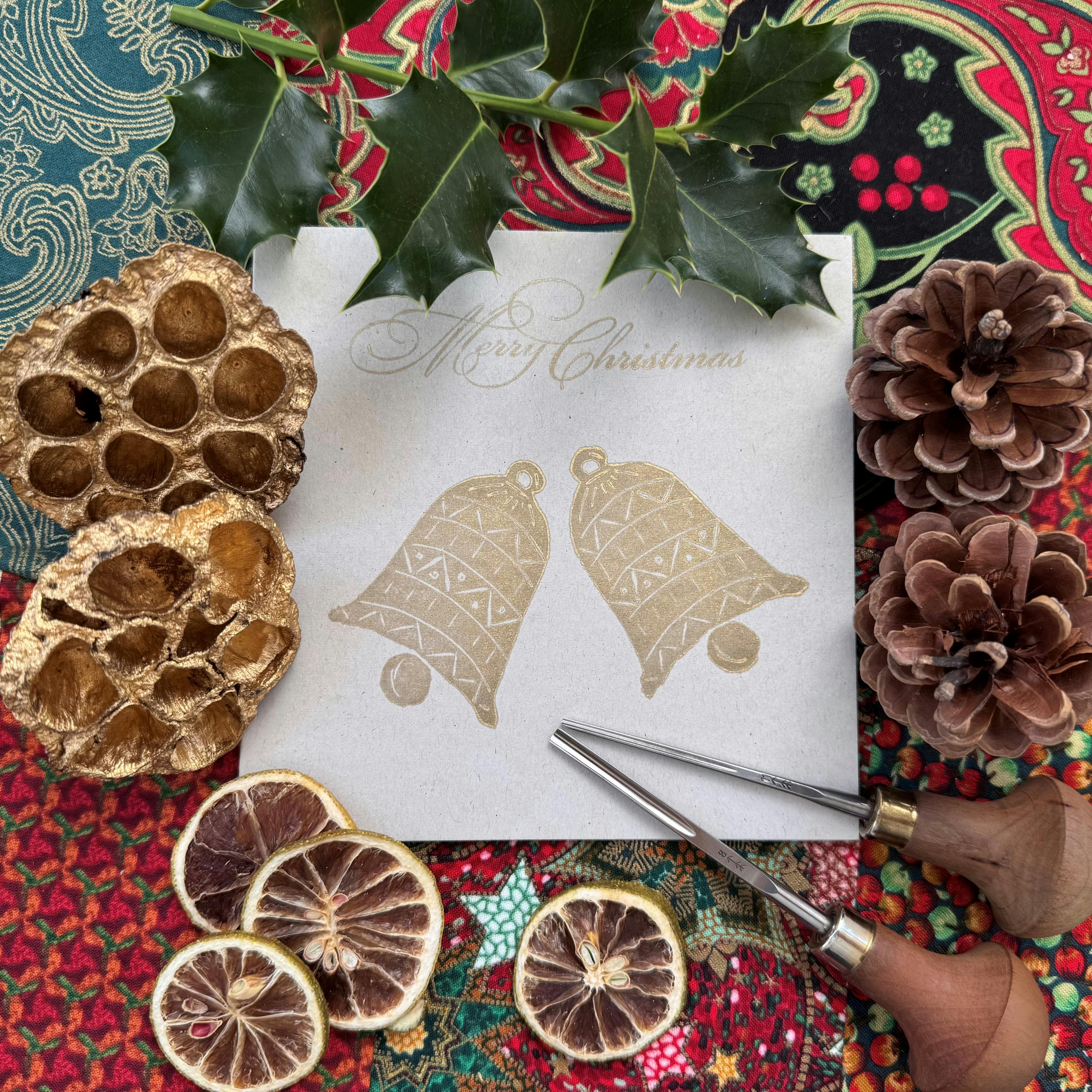 Image shows a gold printed Christmas bells card with holly and winter decorations around it