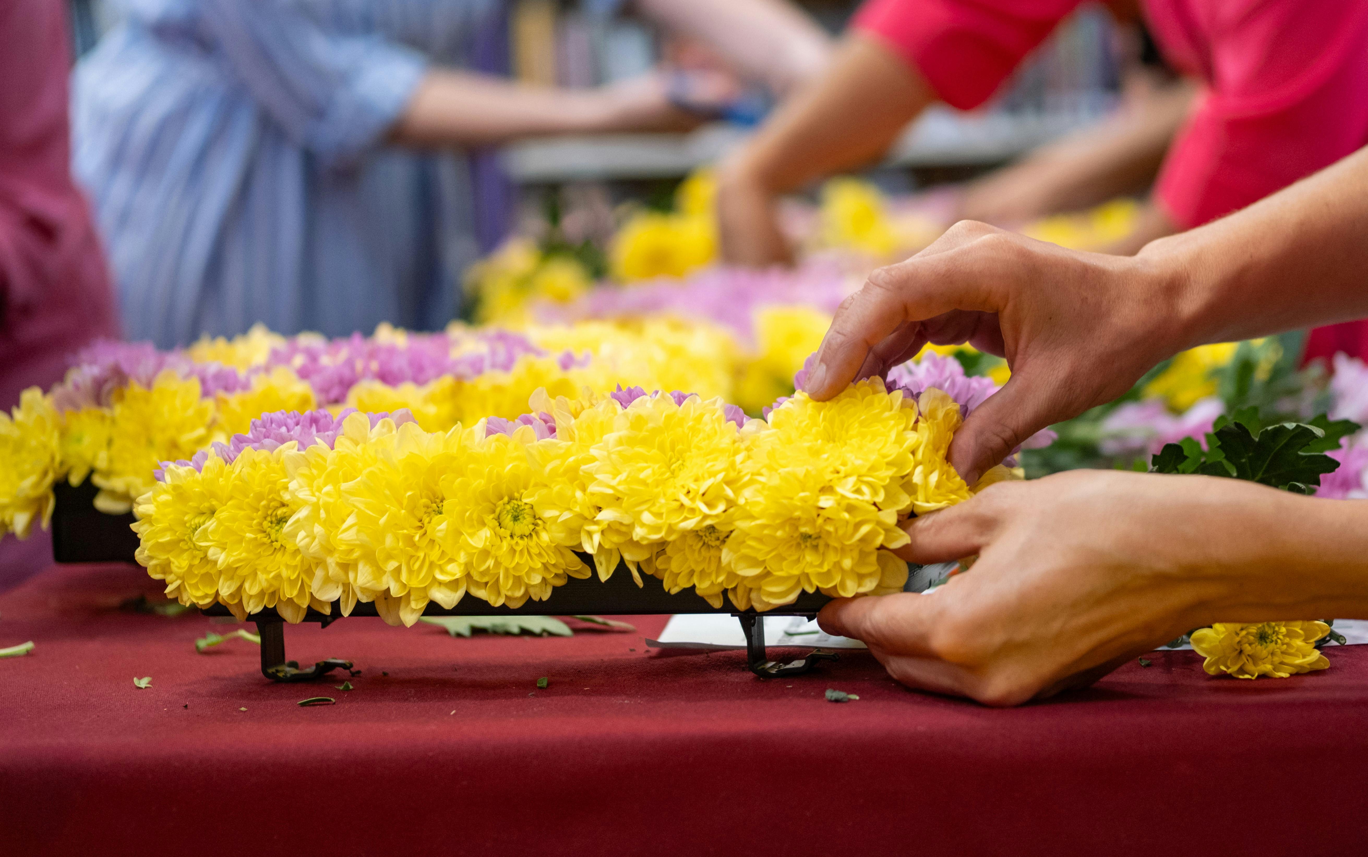 Image of people arranging a floral tribute of yellow and purple flowes