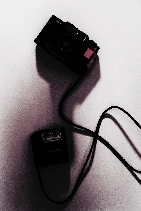 Voigtlander Vito film camera with red tape attached, connected by a cable to a compact Voigtlander flash unit on a light background.