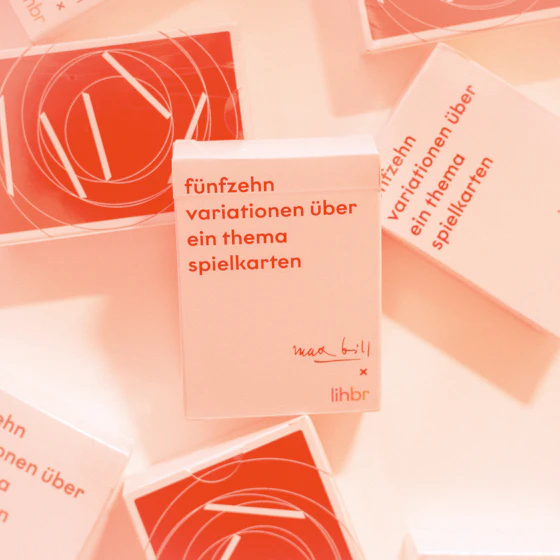 Box of “fünfzehn variationen über ein thema spielkarten” playing cards, surrounded by scattered cards featuring geometric red and white graphic designs. Red-orange filter overlay.