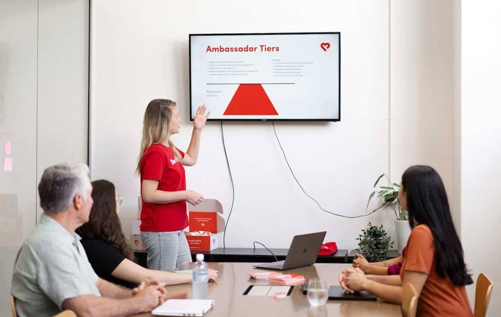 A group of people pose for a photo in an office. A range of ages, genders and ethnicities is represented.