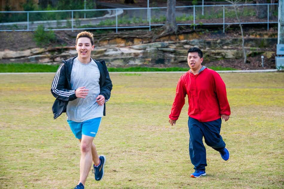 A Like Family Social Carer and Member running on a grassy oval