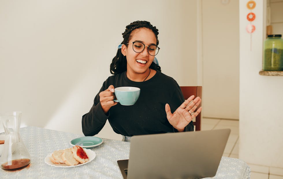 A woman enjoys a tea and toast while sitting in front of her laptop during a video call
