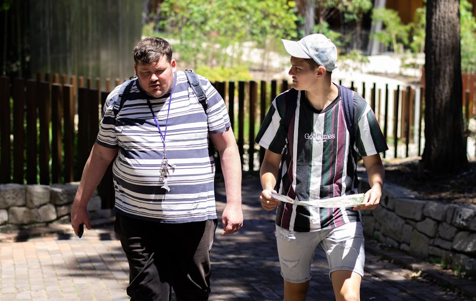 Two men in striped shirts walking side by side. The one on the right holds a map.