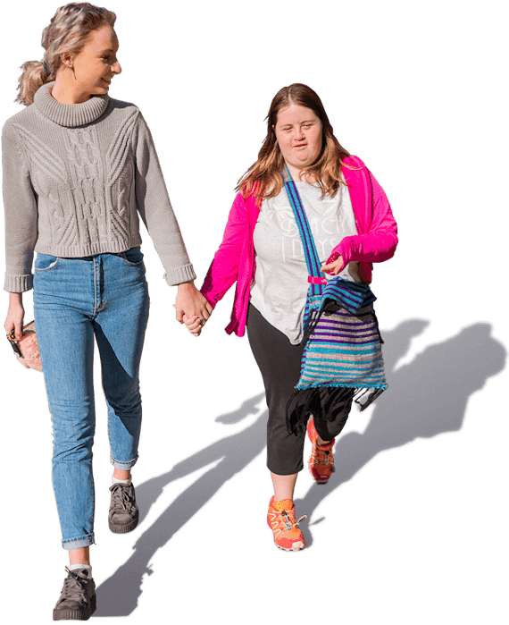 Two young women, one a social carer and one with a disability, walking together holding hands.