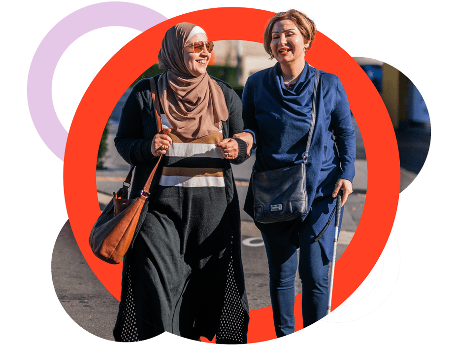 A Like Family Social Carer and Member with their arms linked. The Member is using a white cane