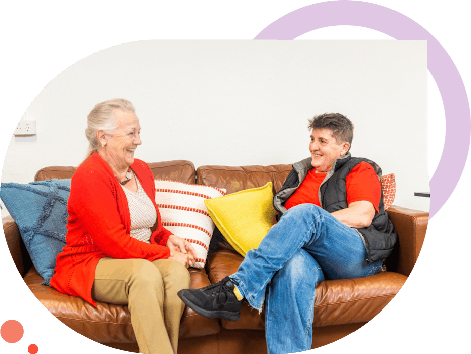 2 women sitting on a brown leather couch facing each other
