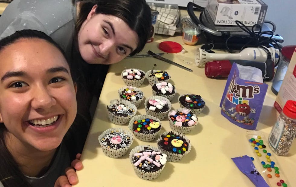 2 young smiling women decorating cupcakes