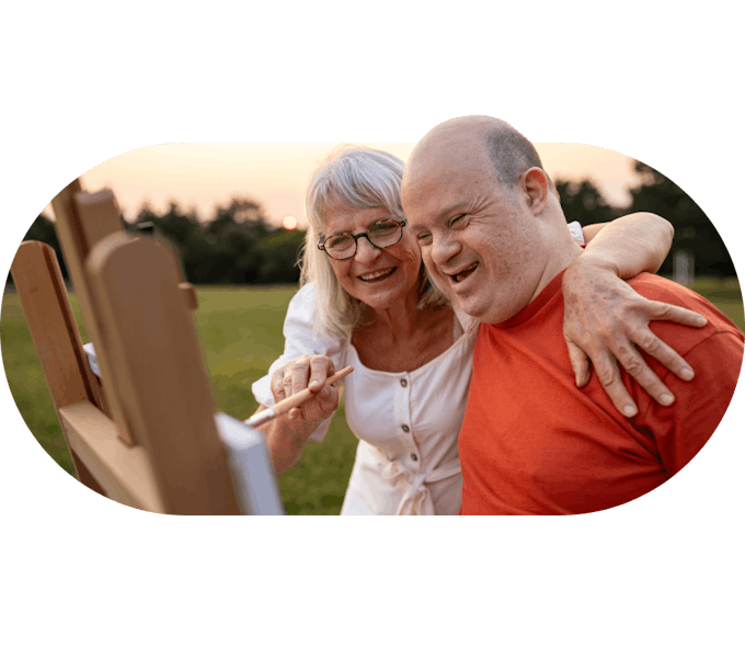 A Member and Carer smiling and painting together outdoors