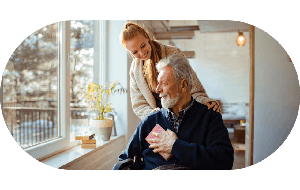 Aged care worker helping an elderly man in a bright house looking out the window