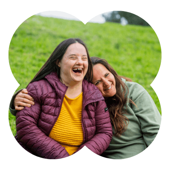 A Member and Social Carer smiling outdoors sitting on grass