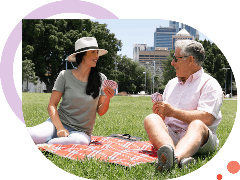 Two people playing cards on a picnic rug in a park