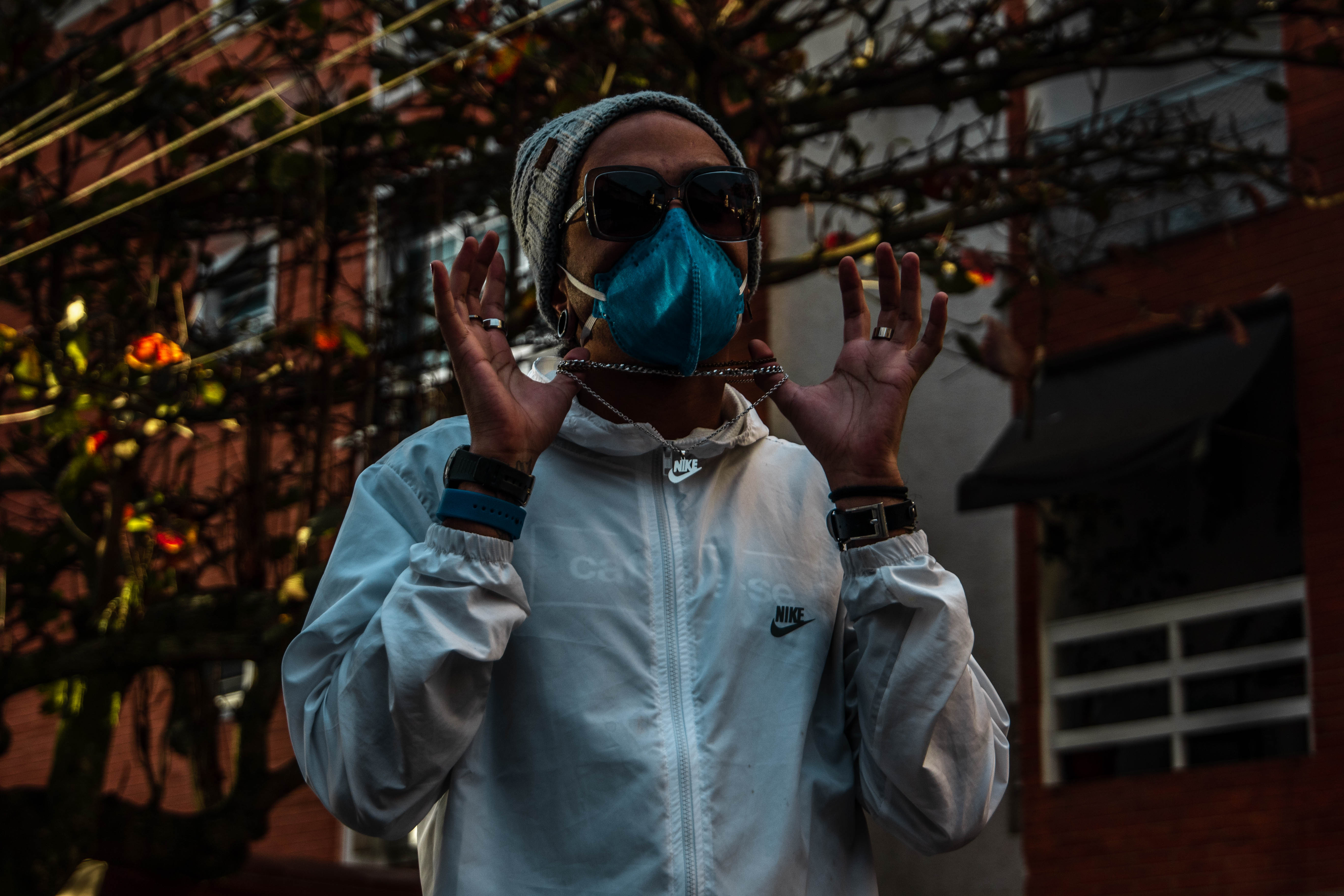 Vidaincerta aparece em uma rua, com jaqueta branca, óculos de sol e máscara PFF2.