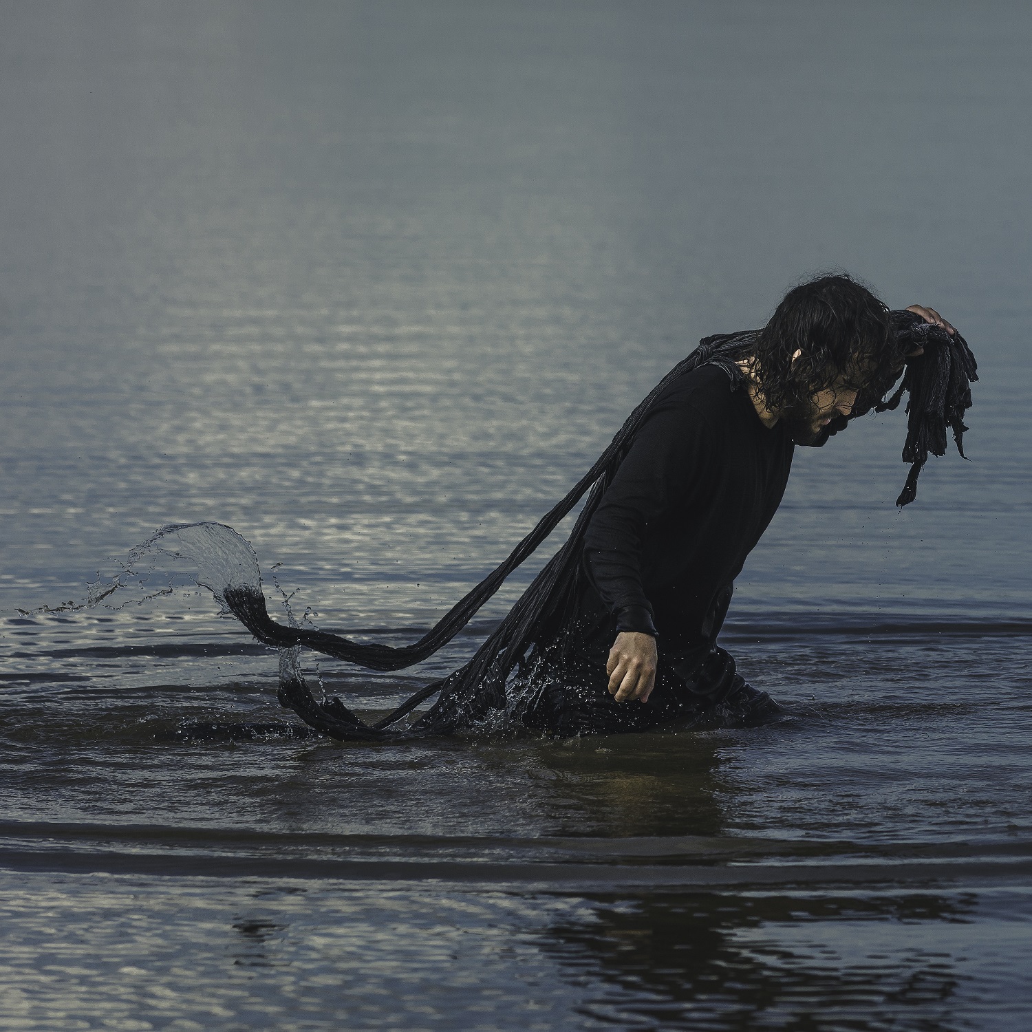 Vito Velasso aparece em frame do vídeo Onde as Dores são Afogadas, dentro do mar, com uma rede de pesca nas costas.