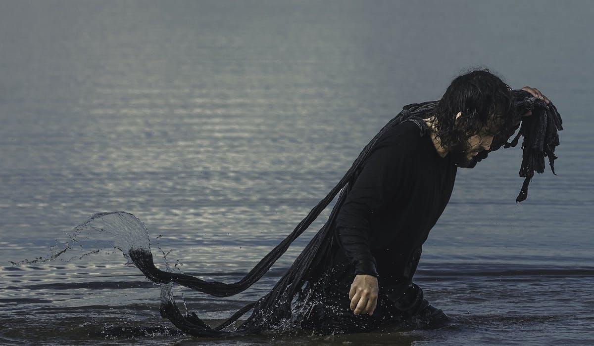 Vito Velasso aparece em frame do vídeo Onde as Dores são Afogadas, dentro do mar, com uma rede de pesca nas costas.