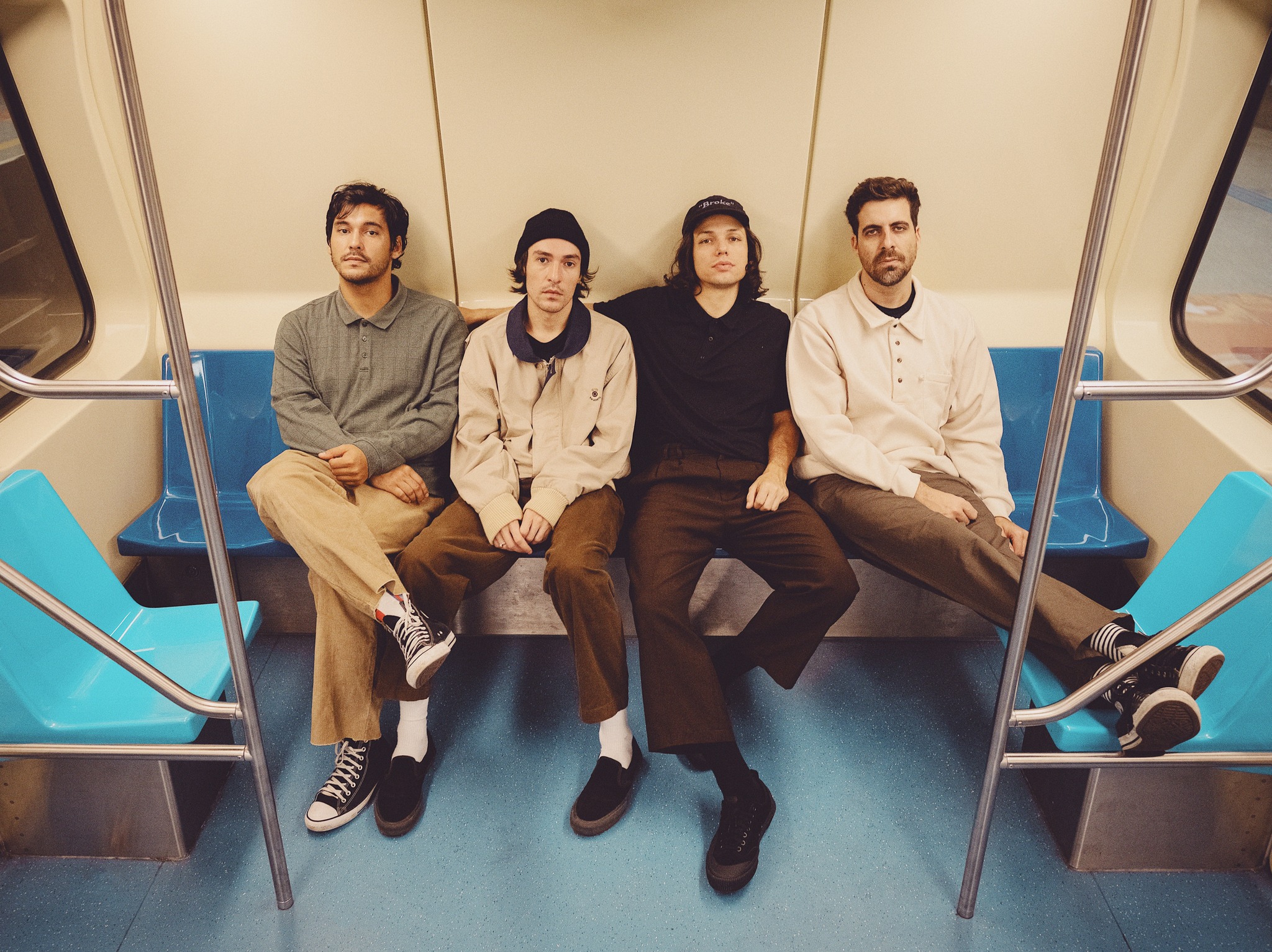 Ale Sater (voz, baixo e violão), Bruno Paschoal (guitarra, baixo, sintetizador e voz), Greg Maya (guitarra e sintetizador) e Luis Cardoso (bateria e voz) sentados no metro de São Paulo. 