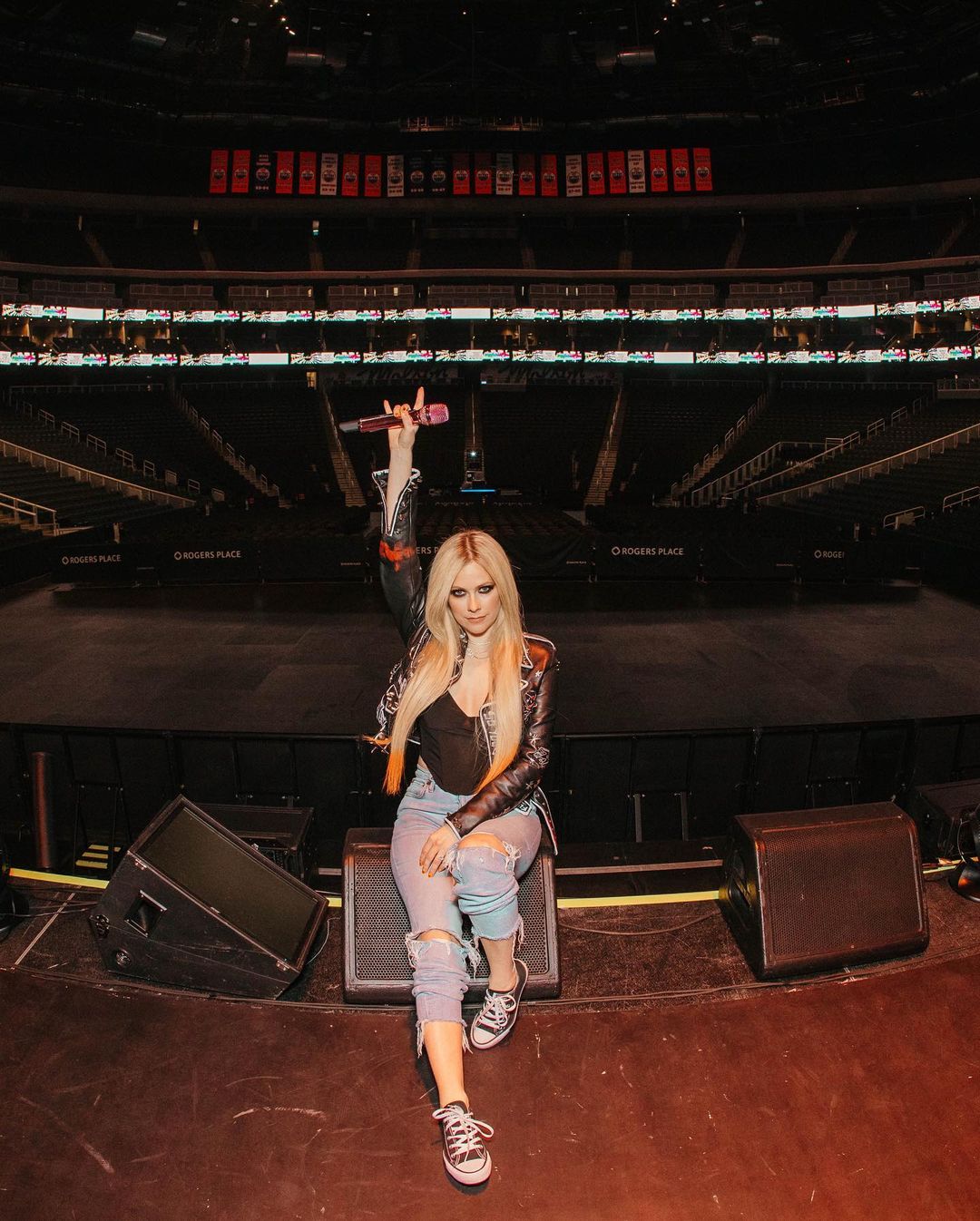 Avril Lavigne em cima do palco, com o microfone erguido