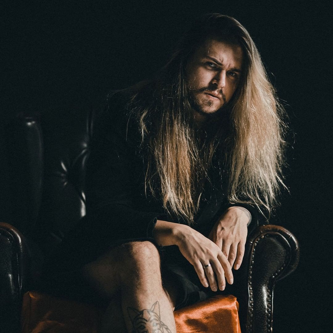 Caio Weber aparece de preto, em um fundo preto, posando para a câmera