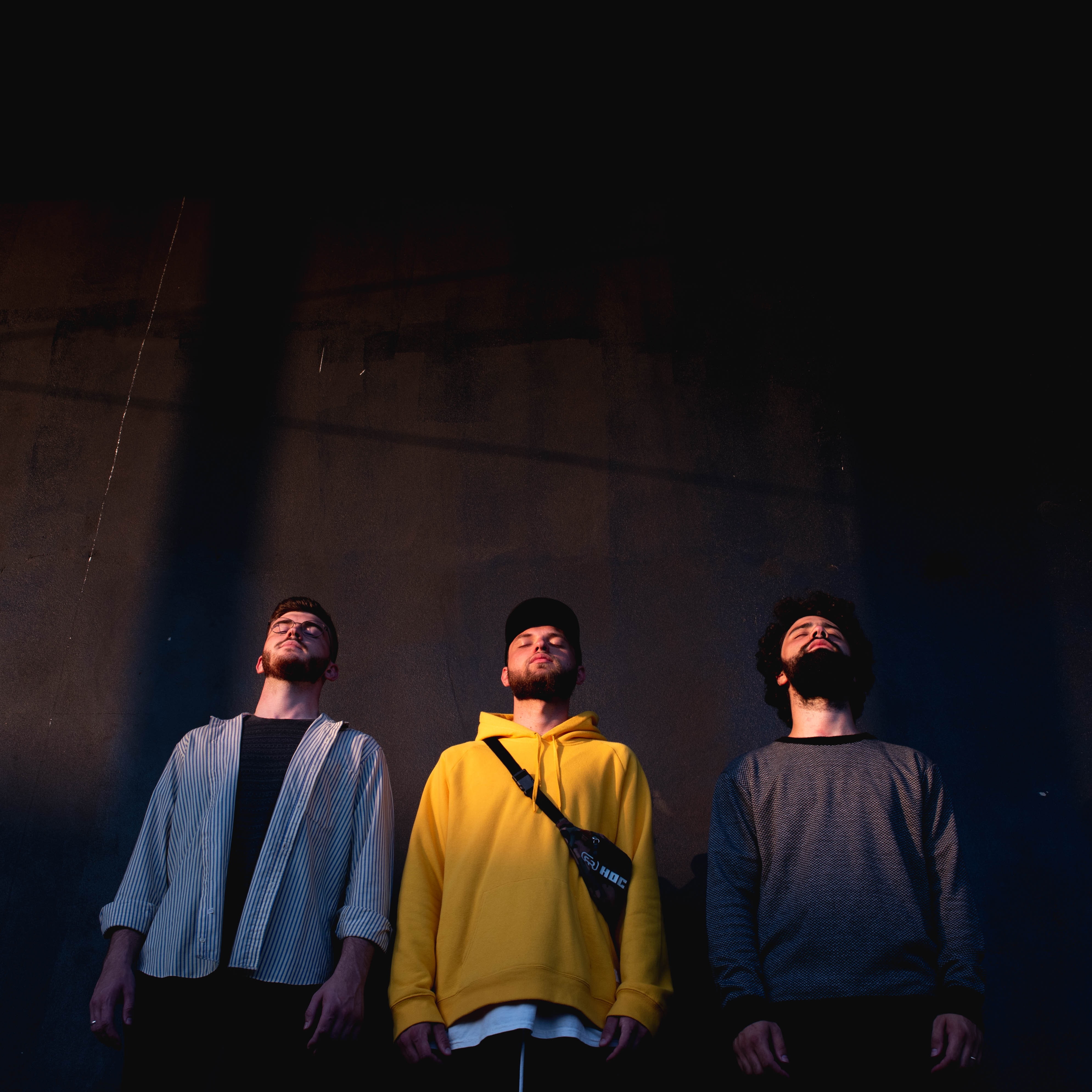 O trio Iago, Kelvyn e Iuri, da esquerda para a direita, está lado a lado. Todos estão com os olhos fechados e mantém a cabeça voltadas para cima.