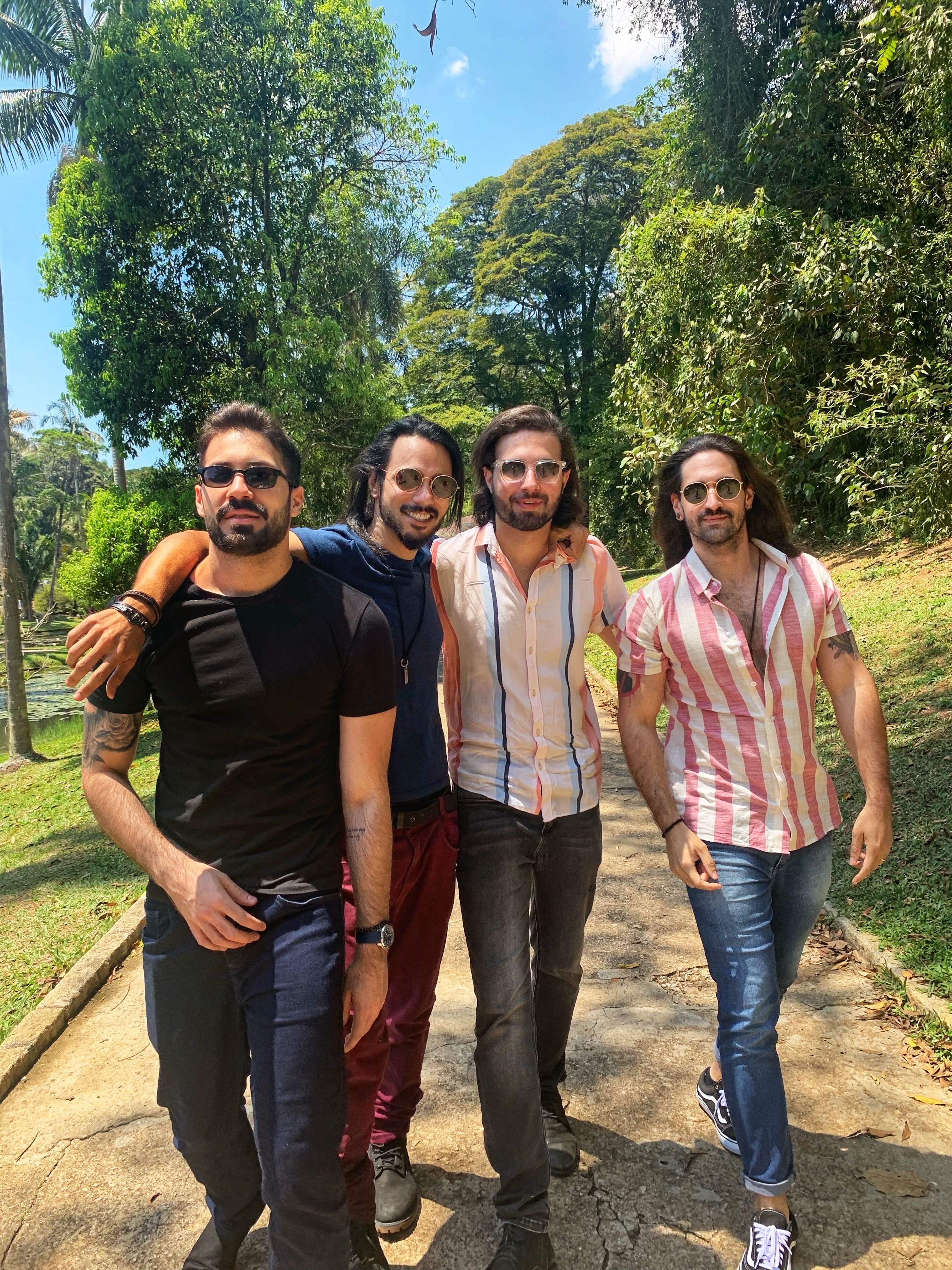 Higor, Bruno, Allan e Tiago em ordem. Lado a lado, eles olham para a câmera. Eles estão em um parque e o sol está forte