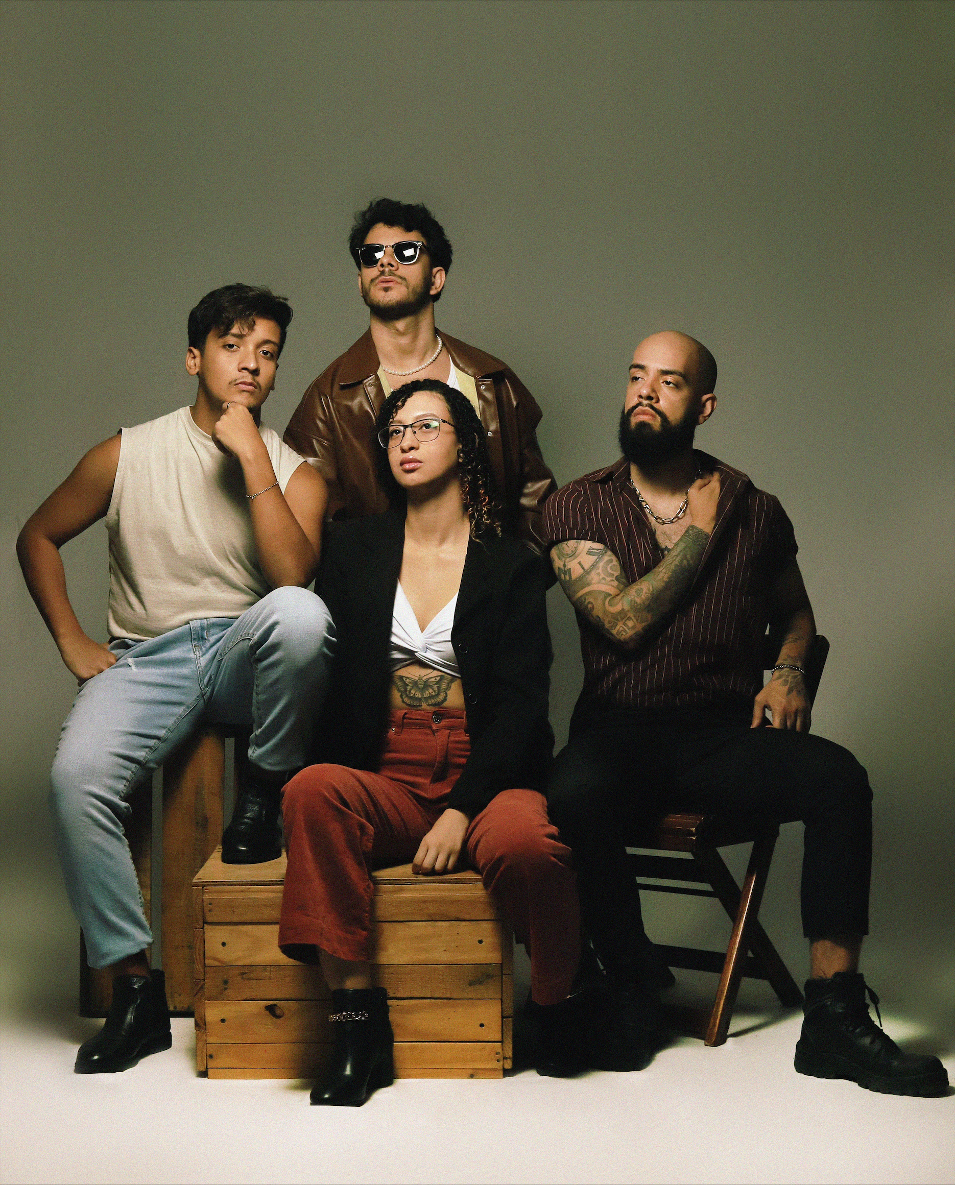 Banda The Lourdes posa para a foto. Três membros estão sentados enquanto Emanuel Gomes está em pé.