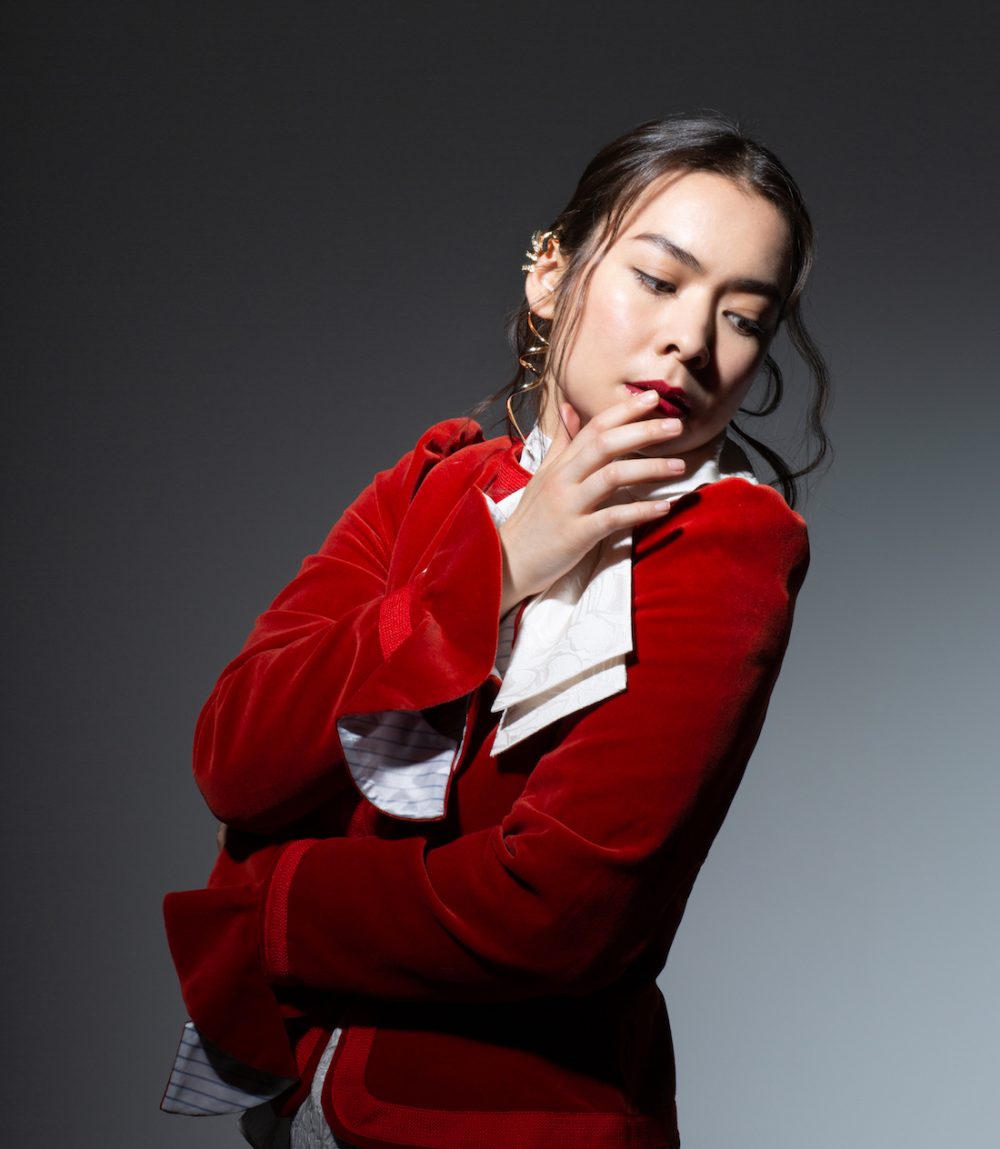 Mitski é uma mulher nipo-americana do cabelo escuro e liso, que está preso atrás de sua cabeça. De vermelho, ela está parcialmente de lado para a foto e olha para baixo.