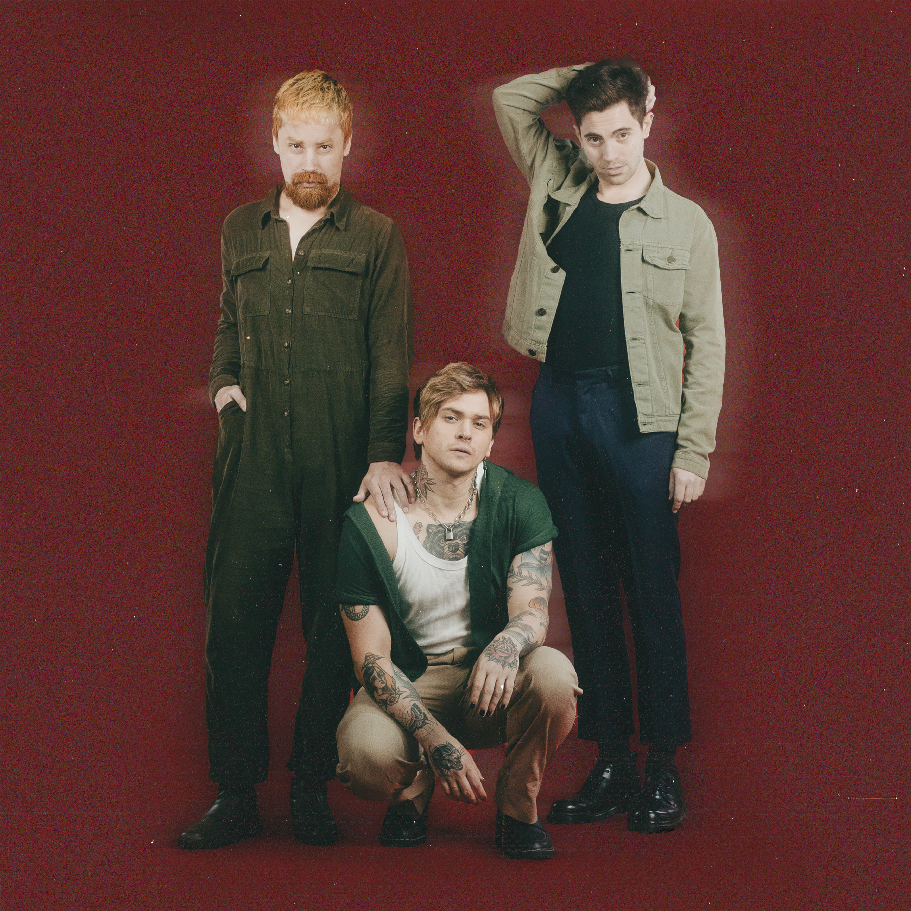 Banda Cefa posa para foto. Enquanto Gabe Oliveira (Guitarra) e Giovani Gonçalves (Baixo) estão em pé, Caio Weber (Vocal) está agachado