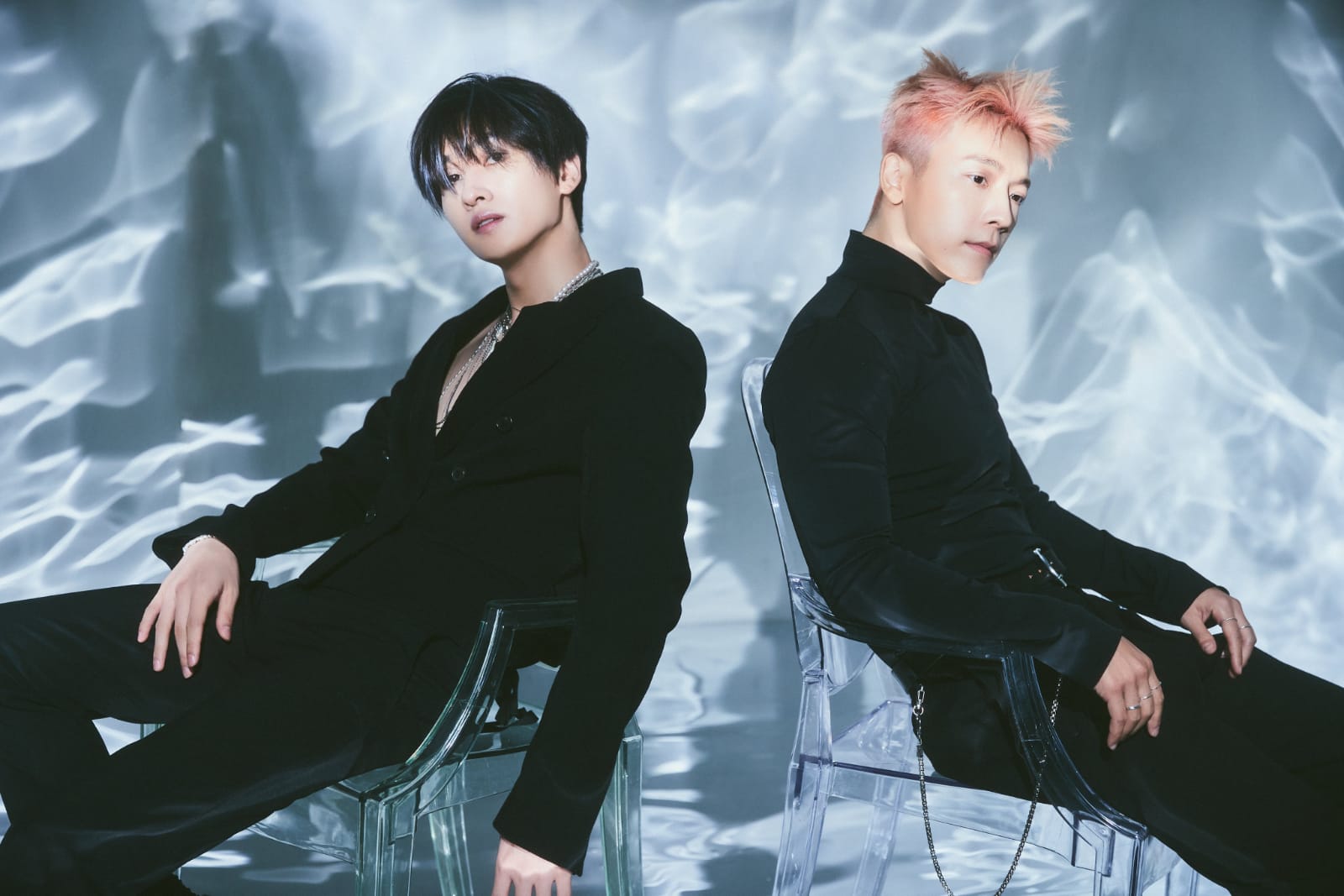 Da esquerda para a direita: Eunhyuk e Donghae. Ambos de preto, estão sentados em uma cadeira transparente em um fundo cintilante.