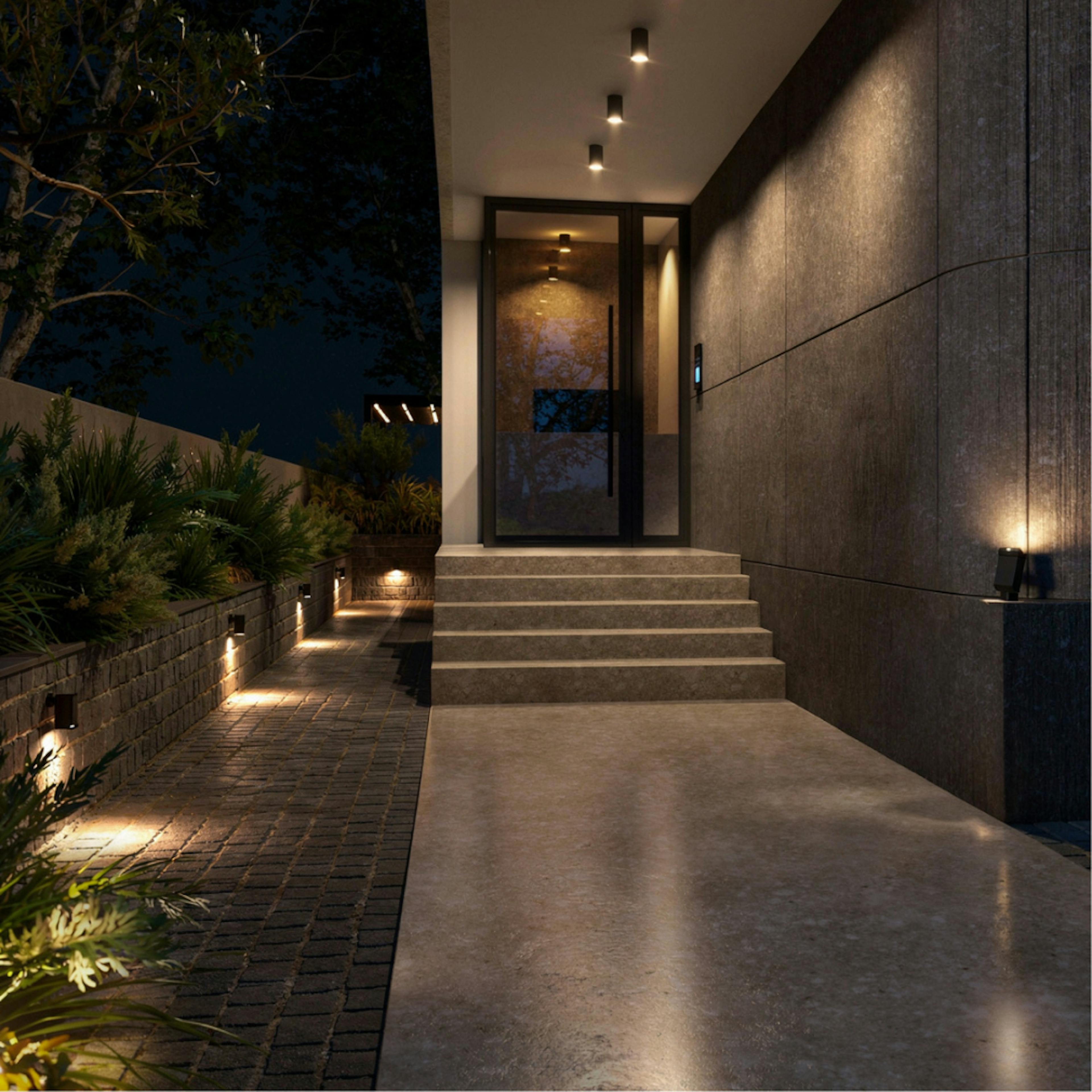 Elegantno osvetljen ulaz u zgradu sa uređenim prilazom i zelenilom